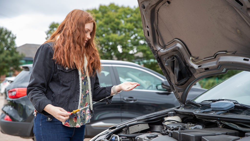 Young lady checking engine oil level on car