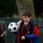 boy holding football walking with two friends