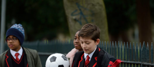 boy holding football walking with two friends