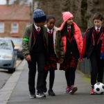 Four children walking down a street kicking a football