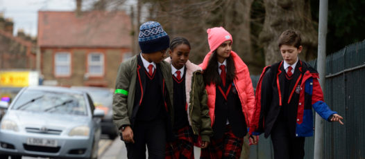 Four children walking down a street kicking a football